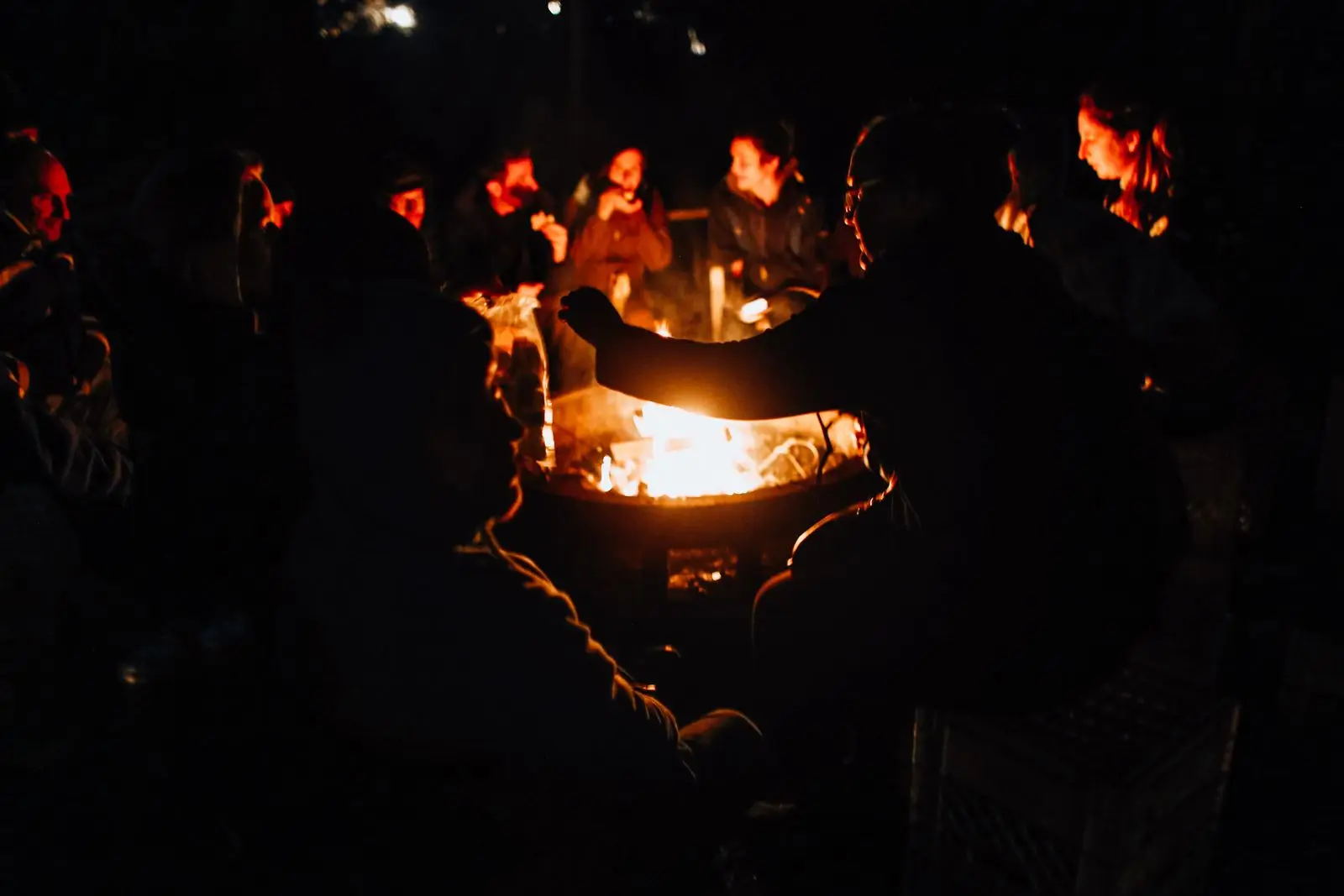 Grupo de personas reunidas alrededor de una fogata de noche