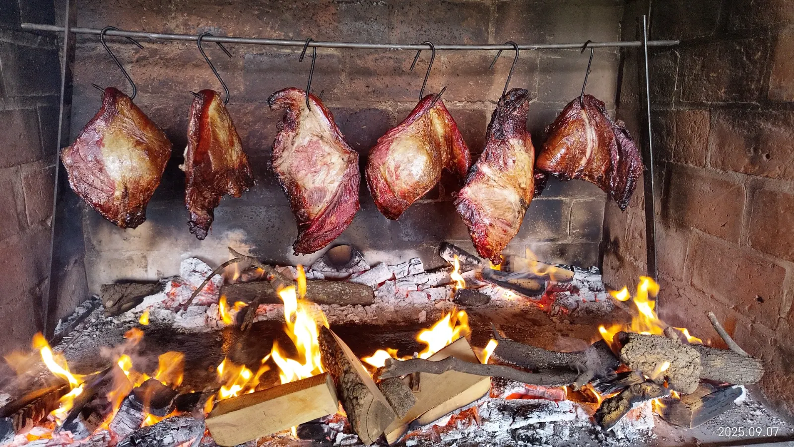 Carnes colgadas al gancho cocinándose sobre el fuego de leña